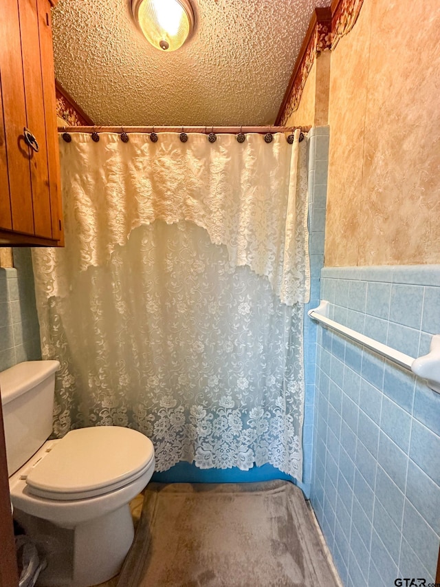 bathroom with curtained shower, toilet, tile walls, and a textured ceiling