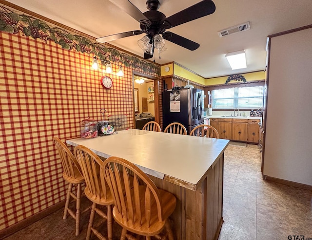 kitchen featuring visible vents, wallpapered walls, a breakfast bar, a sink, and fridge with ice dispenser