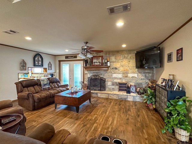 living room featuring visible vents, a stone fireplace, crown molding, and wood finished floors