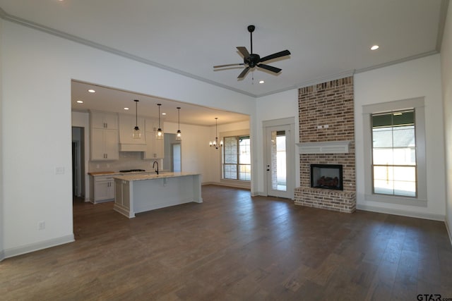 unfurnished living room with ceiling fan with notable chandelier, dark hardwood / wood-style flooring, ornamental molding, and a fireplace