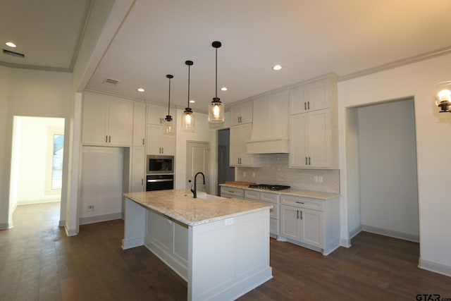 kitchen with black appliances, light stone countertops, white cabinets, sink, and a center island with sink