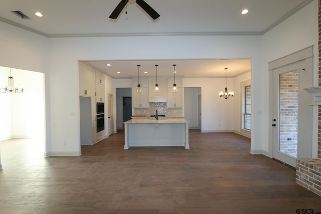 kitchen with tasteful backsplash, white cabinetry, sink, decorative light fixtures, and an island with sink