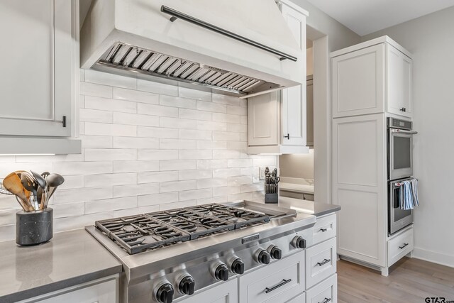 7612 Crosswater, Tyler, TX 75703 - kitchen featuring premium range hood, stainless steel appliances, decorative backsplash, white cabinets, and light wood-style flooring