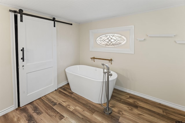 bathroom featuring a soaking tub, baseboards, wood finished floors, and ornamental molding