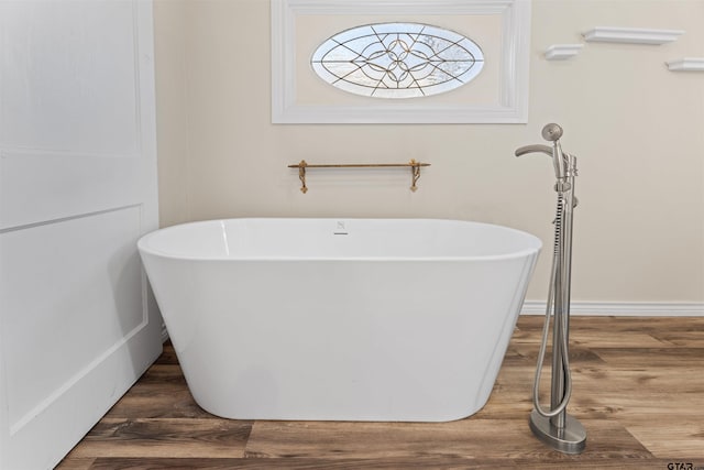 full bathroom featuring baseboards, a freestanding bath, and wood finished floors