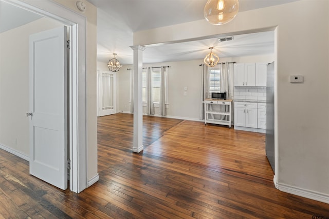 unfurnished living room with dark wood-style floors, a notable chandelier, decorative columns, and visible vents