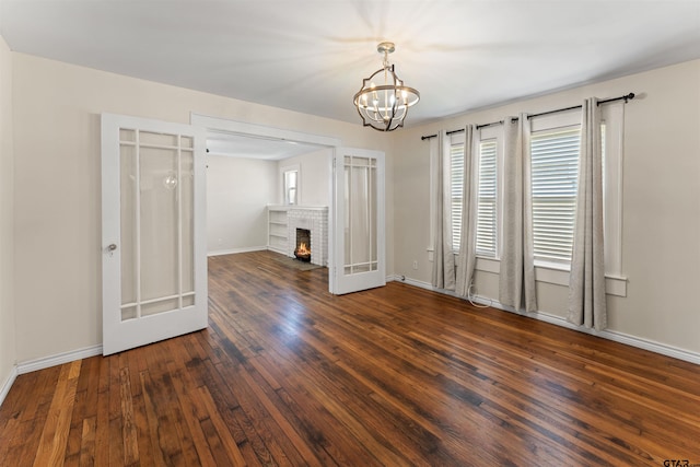 empty room featuring hardwood / wood-style flooring, plenty of natural light, a brick fireplace, and baseboards