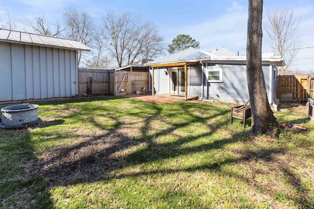 back of house featuring a lawn, a gate, a patio area, metal roof, and a fenced backyard