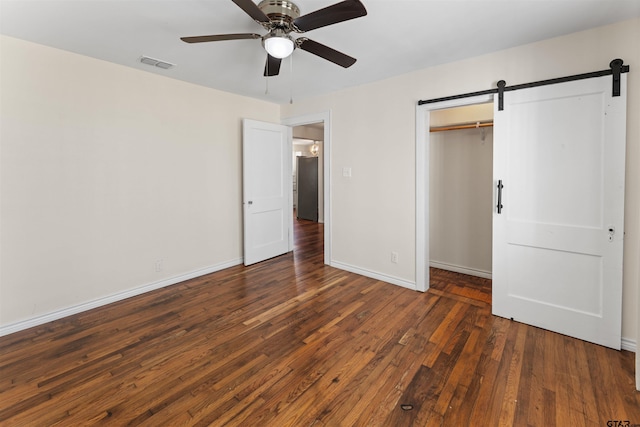 unfurnished bedroom featuring a closet, wood-type flooring, visible vents, a barn door, and baseboards