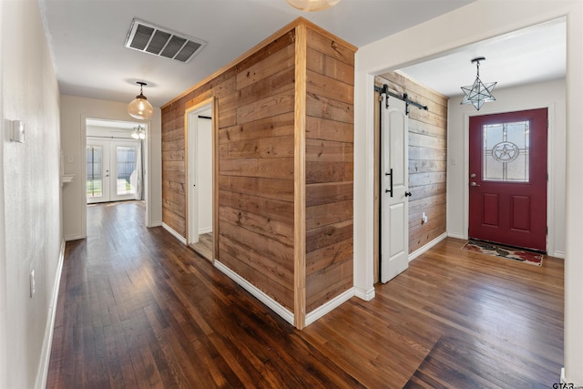 entryway featuring dark wood-style floors, a barn door, wooden walls, and visible vents