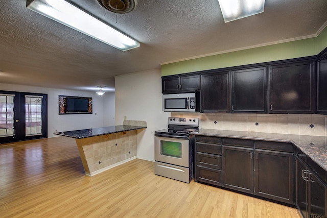 kitchen with crown molding, appliances with stainless steel finishes, a textured ceiling, dark stone countertops, and light hardwood / wood-style flooring