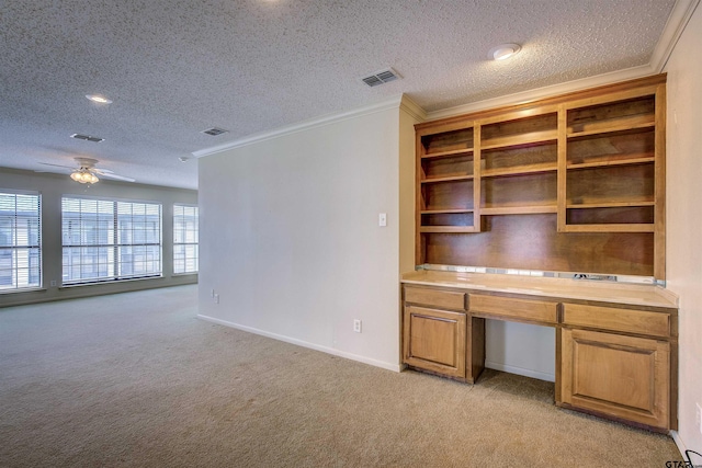 unfurnished office with built in desk, ceiling fan, a textured ceiling, crown molding, and light colored carpet