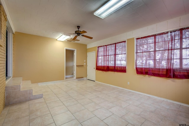 empty room featuring light tile patterned floors, ceiling fan, and brick wall