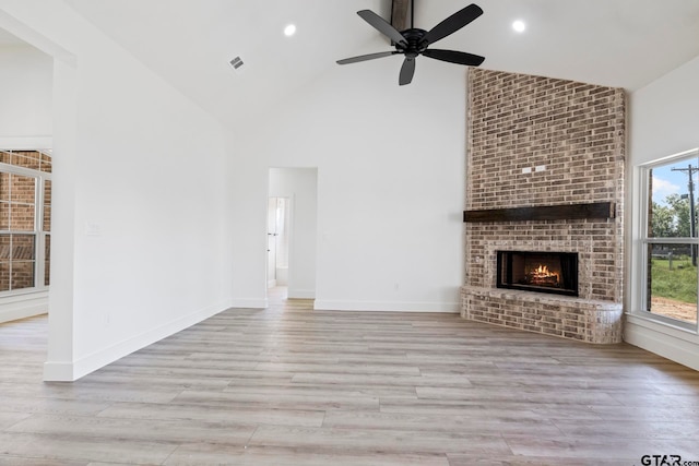 unfurnished living room with ceiling fan, light wood-type flooring, high vaulted ceiling, and a brick fireplace