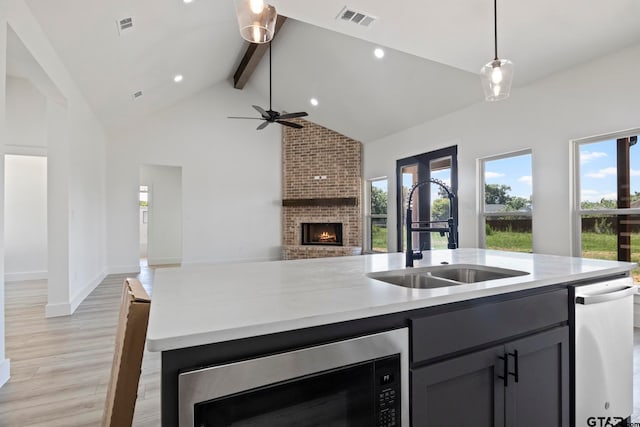 kitchen with pendant lighting, sink, a brick fireplace, light wood-type flooring, and beam ceiling