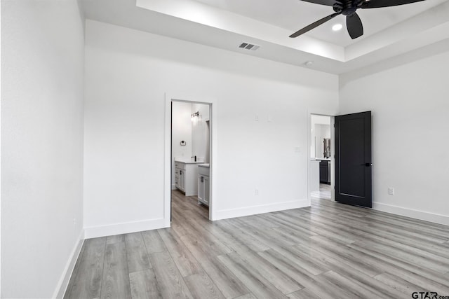 unfurnished bedroom with connected bathroom, ceiling fan, a towering ceiling, light hardwood / wood-style floors, and a tray ceiling