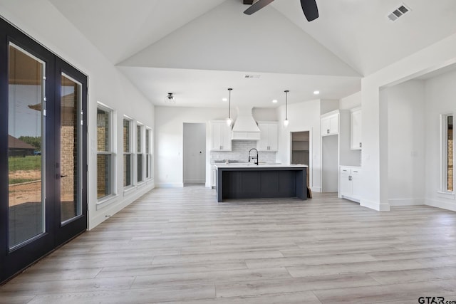 kitchen with decorative light fixtures, a center island with sink, white cabinetry, and light hardwood / wood-style floors