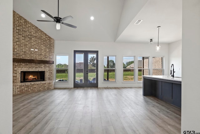 unfurnished living room featuring ceiling fan, sink, a brick fireplace, high vaulted ceiling, and light wood-type flooring