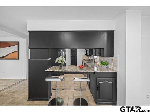 kitchen featuring ornamental molding, a sink, freestanding refrigerator, a kitchen bar, and baseboards