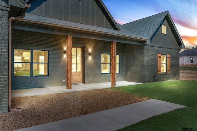 back house at dusk with a lawn and a porch