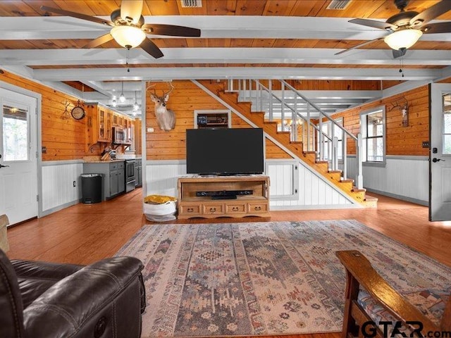 living room featuring hardwood / wood-style floors, beam ceiling, wooden walls, and ceiling fan