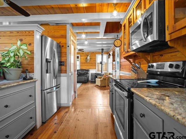 kitchen with appliances with stainless steel finishes, stone countertops, wooden walls, beamed ceiling, and light hardwood / wood-style flooring