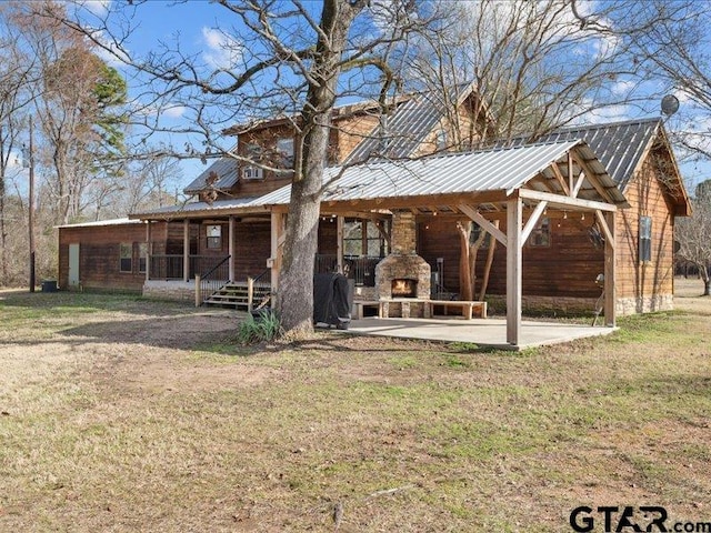 back of property featuring a yard, a patio, and an outdoor stone fireplace