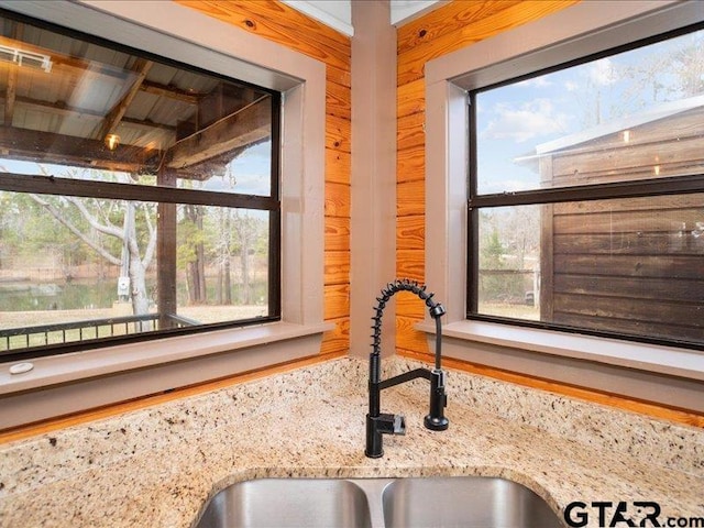 interior details with sink, wooden walls, and light stone countertops