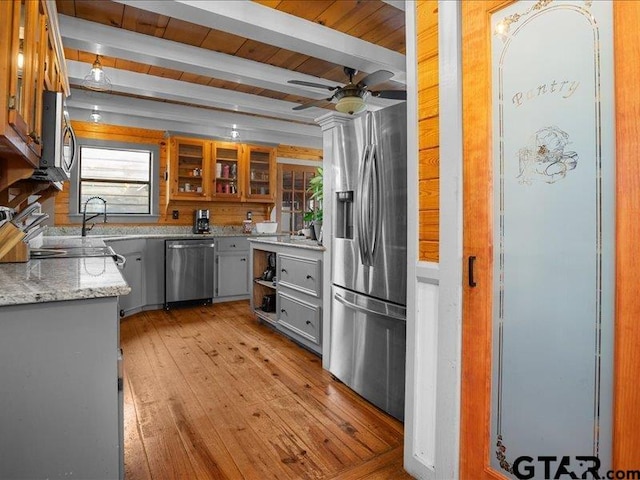 kitchen with gray cabinetry, light hardwood / wood-style flooring, stainless steel appliances, beam ceiling, and light stone countertops