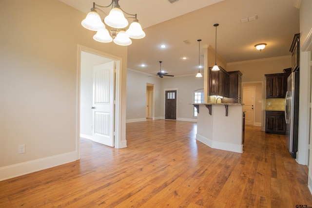 kitchen with pendant lighting, ceiling fan with notable chandelier, stainless steel fridge, wood-type flooring, and a breakfast bar area