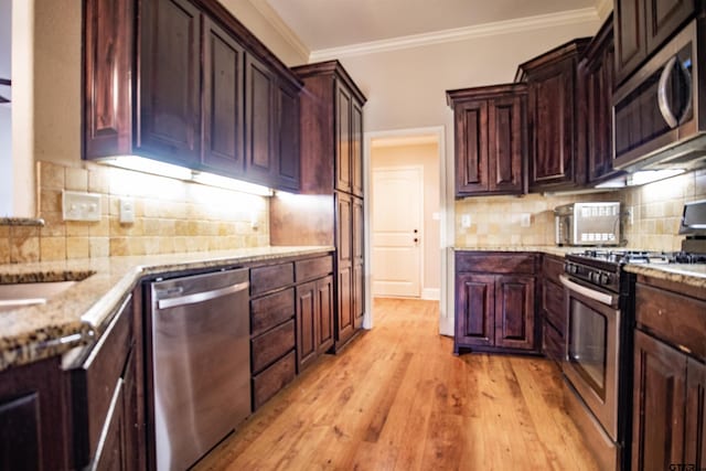 kitchen with decorative backsplash, light stone countertops, light wood-type flooring, ornamental molding, and stainless steel appliances