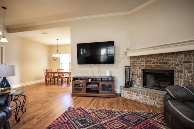 living room featuring a fireplace, wood-type flooring, an inviting chandelier, and crown molding