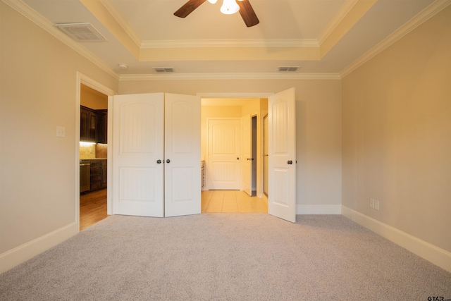 unfurnished bedroom featuring ceiling fan, a raised ceiling, crown molding, and light carpet