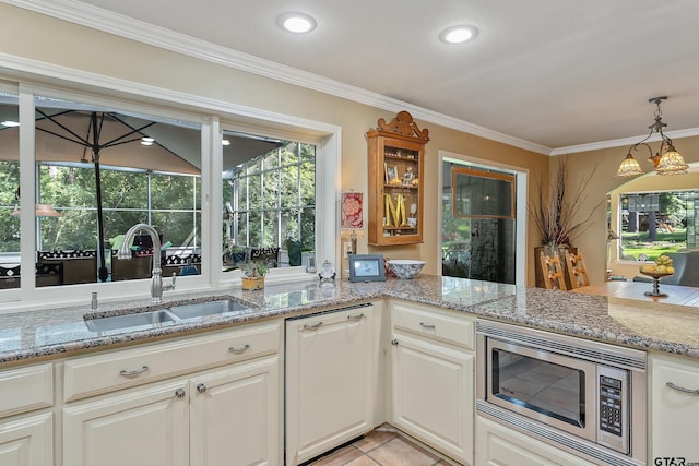 kitchen featuring light stone counters, stainless steel microwave, hanging light fixtures, sink, and crown molding