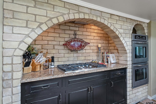 kitchen featuring stainless steel appliances, light stone counters, brick wall, and crown molding