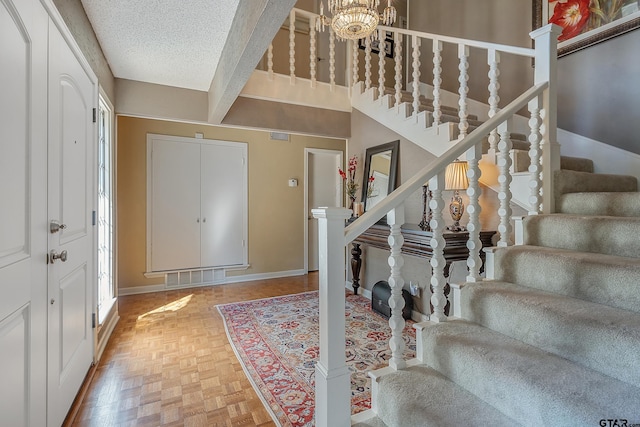 foyer entrance featuring beamed ceiling, a textured ceiling, an inviting chandelier, and parquet floors