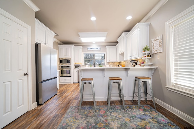 kitchen with kitchen peninsula, appliances with stainless steel finishes, dark hardwood / wood-style flooring, white cabinetry, and a breakfast bar area