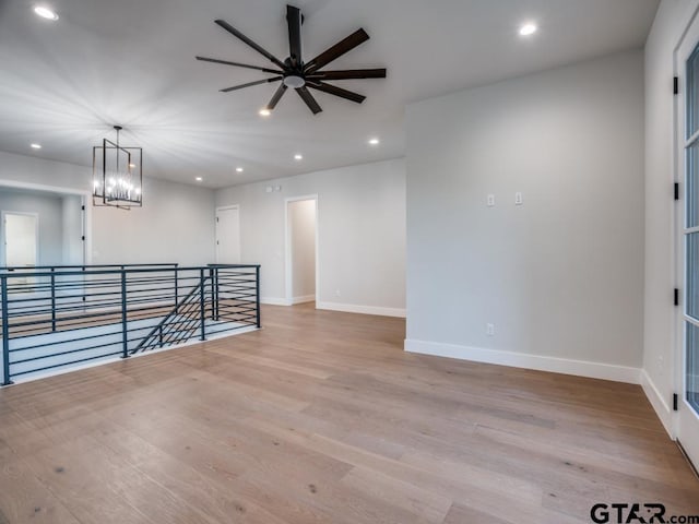 unfurnished room featuring ceiling fan with notable chandelier and light hardwood / wood-style floors