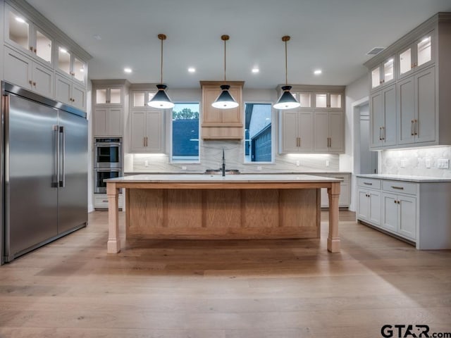 kitchen with stainless steel appliances, pendant lighting, a kitchen island, and light wood-type flooring