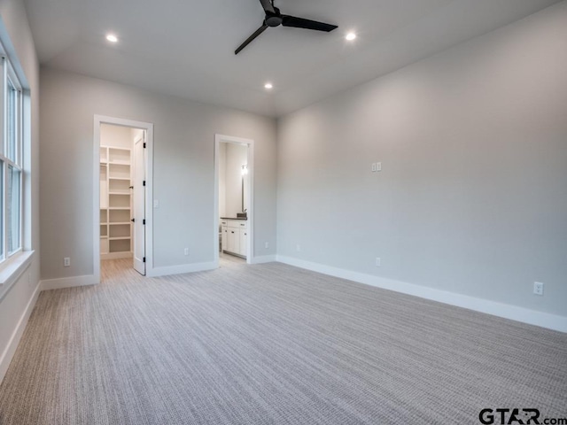 unfurnished bedroom featuring light carpet, ensuite bathroom, ceiling fan, a walk in closet, and a closet