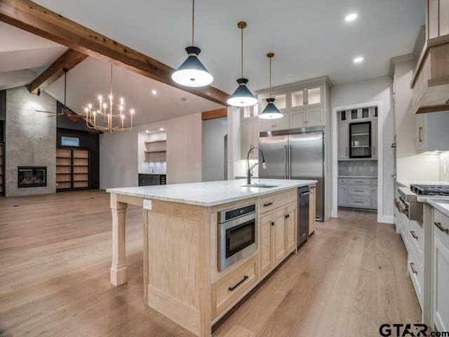 kitchen with lofted ceiling with beams, appliances with stainless steel finishes, decorative light fixtures, a large island, and light hardwood / wood-style floors