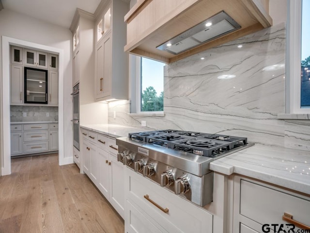 kitchen with appliances with stainless steel finishes, custom exhaust hood, backsplash, light hardwood / wood-style flooring, and white cabinets