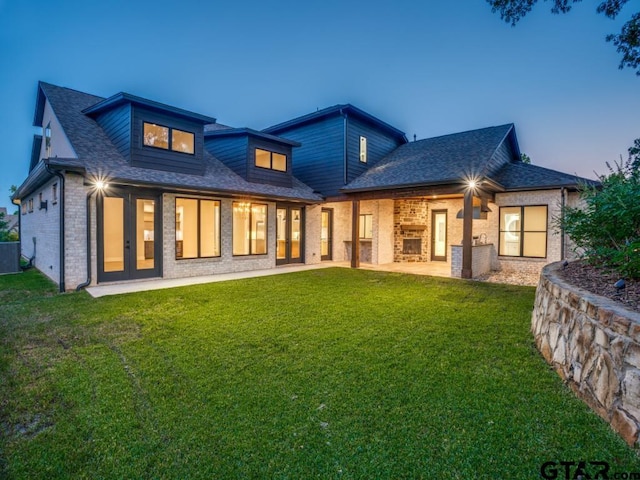 back house at dusk with a patio, a yard, and french doors