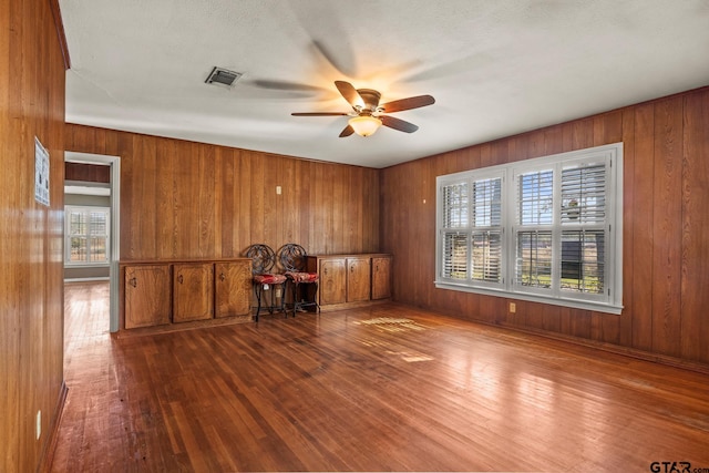 interior space with a wealth of natural light, wooden walls, hardwood / wood-style flooring, and ceiling fan