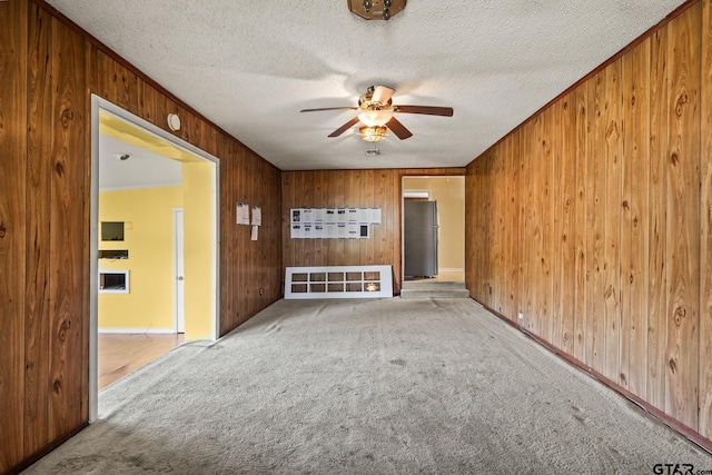 unfurnished living room with ceiling fan, light colored carpet, wooden walls, and ornamental molding