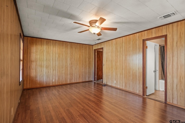 spare room featuring wood walls, wood-type flooring, and ceiling fan