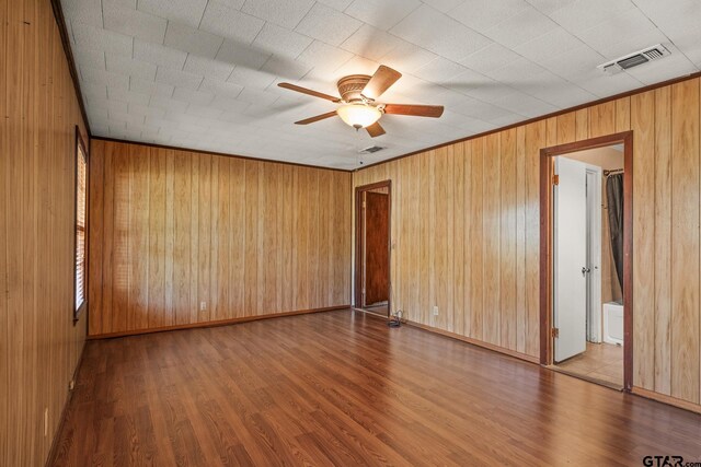 spare room featuring wood walls, wood-type flooring, and ceiling fan