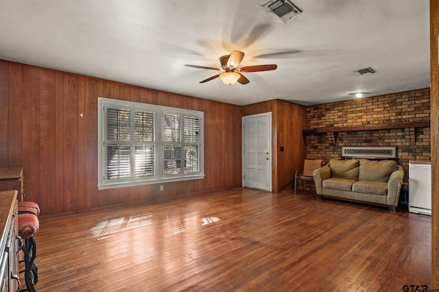 living room featuring wooden walls, a textured ceiling, hardwood / wood-style flooring, and a brick fireplace