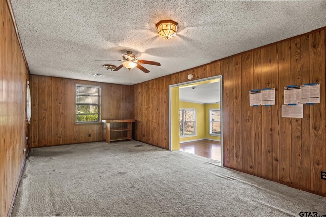 spare room featuring a textured ceiling, light colored carpet, and wooden walls