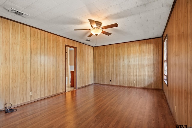 empty room with wooden walls, hardwood / wood-style flooring, and ceiling fan